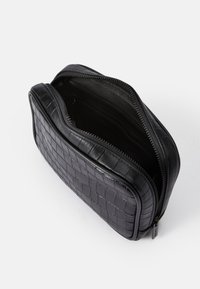 Črn usnjen etui s kviltano teksturo, zadrgo in gladkim notranjim delom s prostori za kartice. Kompaktna pravokotna oblika.