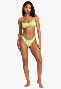 Light green bikini with a ruched top and floral print on the bottoms. Adjustable straps and a minimal design emphasizing a fitted silhouette.