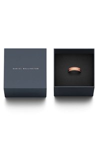 Roségoldener Ring in einer dunkelblauen quadratischen Box. Die Box hat goldenen "DANIEL WELLINGTON"-Text und ein weiches schwarzes Innenleben. Der Ring hat ein elegantes Design.