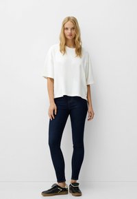 Vit oversized t-shirt med sänkt axel, i kombination med mörka skinny jeans och svarta sneakers med en ljus accent. Enkelt mönster, avslappnad passform.