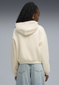 Sudadera crema con capucha, corte holgado, hombros caídos y dobladillo acanalado. Combinada con pantalones vaqueros de pierna ancha en azul claro.