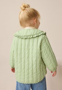 Grüne gesteppte Gingham-Jacke mit gerafftem Kragen und elastischen Bündchen, mit glattem Stoff und lockerem Schnitt, kombiniert mit blauen Jeans.