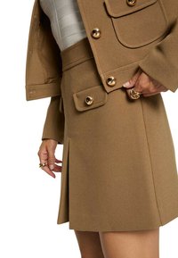 Conjunto de chaqueta y falda marrón a medida con botones dorados, bolsillos de solapa y una textura suave con un ligero pliegue en la falda.