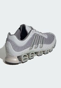 Grauer Sportschuh mit Mesh-Obermaterial, Kunststoffakzenten und einzigartiger gepolsterter Sohle. Verfügt über drei Seitenstreifen und einen gepolsterten Kragen für zusätzlichen Halt.