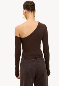 Haut marron asymétrique à manches longues avec un col en U, une texture douce et un détail de froncement. Associé à un jean foncé taille haute.