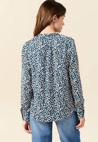 Marineblaue Langarmbluse mit einem weißen abstrakten Muster, Knopfmanschetten und einer leichten Falte im Rücken für einen entspannten Sitz.