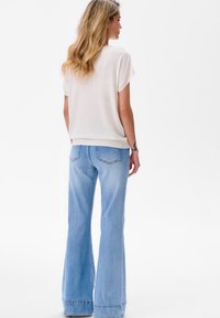 Hellbeige, oversized Sweater mit kurzen Ärmeln, kombiniert mit hellblauen Schlagjeans mit Gesäßtaschen und einer bequemen Waschung.