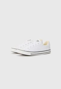 Hvite lerrets sneakers med lav design, snøring og svart gummisåle. Har sølvfargede øyelets og en teksturert tåhette.