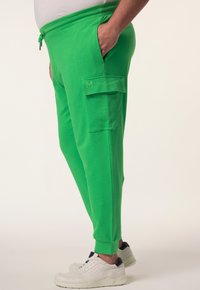 Groene fleece joggers met een cargozak en elastische tailleband. Gecombineerd met witte sneakers, met een ronde neus en zwarte accenten.