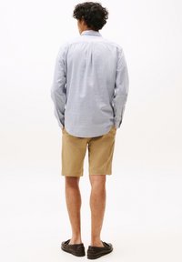 Lichtblauw geruite langarmshirt, beige shorts, zwarte instappers. Katoenmengsel, relaxed fit, achterkant met plooi-detail. Neutrale achtergrond.
