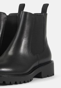 Bottes Chelsea en cuir noir avec panneaux latéraux élastiques, languettes à l'arrière et semelles épaisses crantées pour adhérence et durabilité.