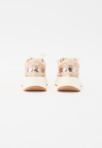 Skoene har en beige mesh-overdel med metallisk detaljering og søm. Sålen er hvit med en beige teksturert finish.
