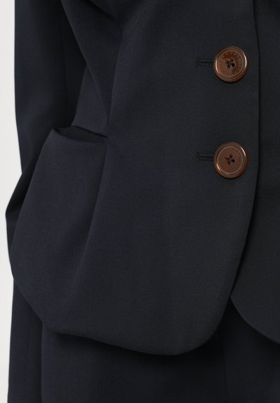 Marineblazer med to brune knapper, en skræddersyet revers og sidelommer. Stoffet har en glat tekstur og en tætsiddende pasform.