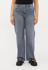 Calças de ganga de perna larga em azul escuro com riscas brancas verticais, apresentando um clássico design de cinco bolsos e detalhes de bainha desfiada.