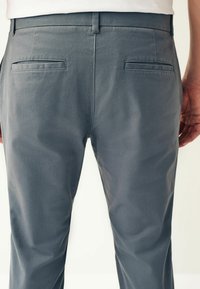 Pantaloni dintr-un material elastic, gri, cu o textură fină, având o croială slim, două buzunare la spate și un buclă pentru curea la talie.