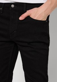 Sorte denimjeans med tætsiddende pasform og klassisk fem-lomme-design. Tekstureret stof med kontraststing og metal-knapdetalje.