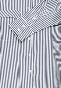Blue and white striped button-up shirt made of cotton, featuring a chest pocket, a button-down collar, and long sleeves with buttoned cuffs.