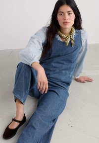 Jeansove kombinacije v temno modri barvi z ravnim krojem, nosijo se čez svetlo modro majico z dolgimi rokavi. Ujemajo se z rjavimi ravnimi čevlji in vzorčasto rutico.