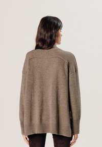 Übergroßer, olivgrüner Pullover mit strukturiertem Strick, hohem Kragen und geripptem Saum. Zeigt eine lockere Passform mit überschnittenen Schulternähten.