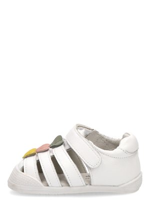 Sandalia blanca para niño pequeño con talón cerrado, tira de velcro, punta abierta y tres decoraciones en forma de hoja en amarillo, rosa y verde en la parte superior.