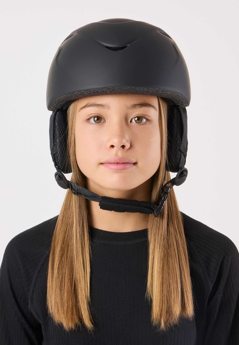 Zwarte helm met ventilatiesleuven en gevoerde oorkappen, bevestigd met een kinbandje. Draagt een persoon met recht, lichtbruin haar.