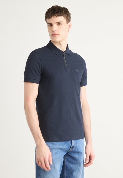 Polo shirt marine à manches courtes, fermeture éclair, et un petit logo brodé sur la poitrine, fabriqué à partir d'un tissu lisse et texturé.