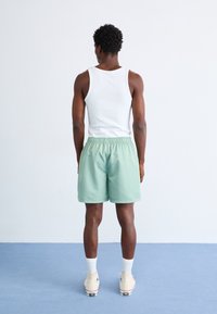 Light green shorts with an elastic waistband, paired with a white tank top and beige high-top shoes. Smooth texture and casual design.