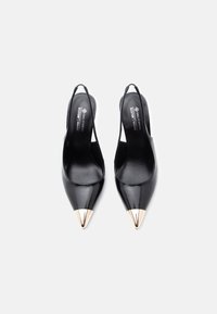 Černé lakované kožené slingback podpatky s špičatými zlatými kovovými akcenty na špičce, s hladkým povrchem a minimalistickým designem.