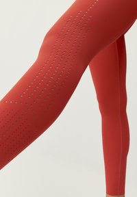 Röda idrottstights med en slät yta, prydda med små skärningar längs sidan för ventilation. Åtsittande design.