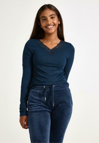 Mørkeblå langærmet top med blonderkantet V-hals og tætsiddende design, kombineret med mørke, bløde sweatpants med elastisk snøre i taljen.