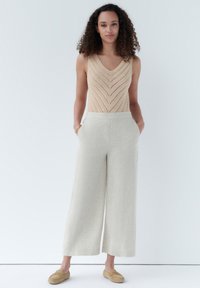 Top in maglia beige con motivo a zigzag, abbinato a pantaloni larghi in lino color crema chiaro e scarpe slip-on color tan.