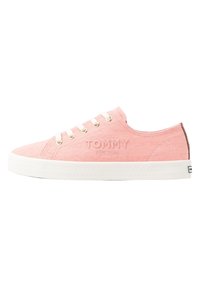 Hellrosa Leinwand-Sneaker mit weißen Schnürsenkeln und goldfarbenen Ösen, versehen mit einem geprägten "TOMMY"-Logo und weißer Gummisohle mit strukturiertem Muster.