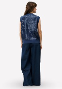 Pull sans manches bleu marine avec un dos orné de sequins, ourlet côtelé, associé à un pantalon en denim foncé à jambes larges.