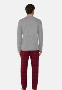 Szary longsleeve w połączeniu z czerwonymi, w kratę spodniami piżamowymi, charakteryzującymi się miękką teksturą i luźnym krojem. Na koszulce brak widocznych wzorów.