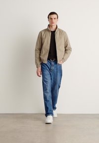 Vaalean beige college-takki, musta paita, siniset farkut ja valkoiset lenkkarit. Sileä kangas, rento istuvuus ja minimalistinen muotoilu.