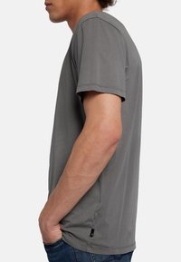 T-shirt grigio a maniche corte, tessuto morbido, scollatura a girocollo, vestibilità rilassata, con un piccolo tag del logo all'orlo, vista laterale.