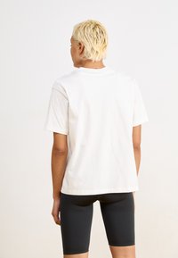 Hvit bomull T-skjorte med korte ermer, avslappet passform, rund halslinning. Kombinert med svarte sykkelshorts, minimalistisk design, glatt tekstur.