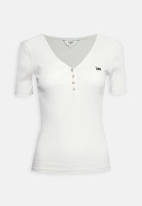 Bílý žebrovaný tričko s krátkým rukávem, výstřihem do V, pěticípým knoflíkovým zapínáním a malým černým vyšitým logem "Lee" na levé straně hrudníku.