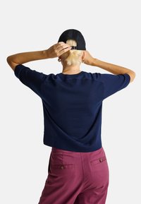 Granatowy sweter dziany z krótkimi rękawami i okrągłym dekoltem. Zestawiony z klasycznymi, wysoko osadzonymi spodniami w kolorze burgundowym z tylnymi kieszeniami.