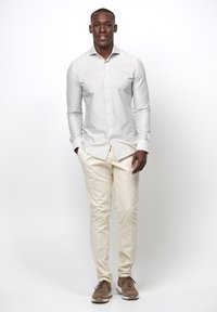 Camisa de botones a rayas en blanco y gris claro, combinada con chinos crema y zapatillas marrones. La camisa tiene mangas largas y un corte a medida.