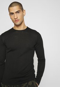 T-shirt noir à manches longues et col ras du cou en tissu léger et côtelé, présentant une coupe ajustée et une texture lisse.
