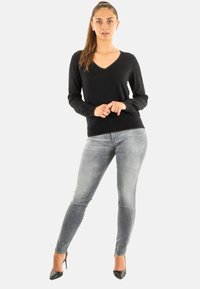 Pull à col en V noir à manches longues associé à un jean slim gris clair et des escarpins noirs. Tissu doux avec un minimalisme dans les détails.