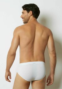 Weiße Baumwollslips mit einem weichen Bund, von der Rückseite gezeigt. Glatte Textur und figurnahes Design. Hautfarbe an den exponierten Stellen sichtbar.