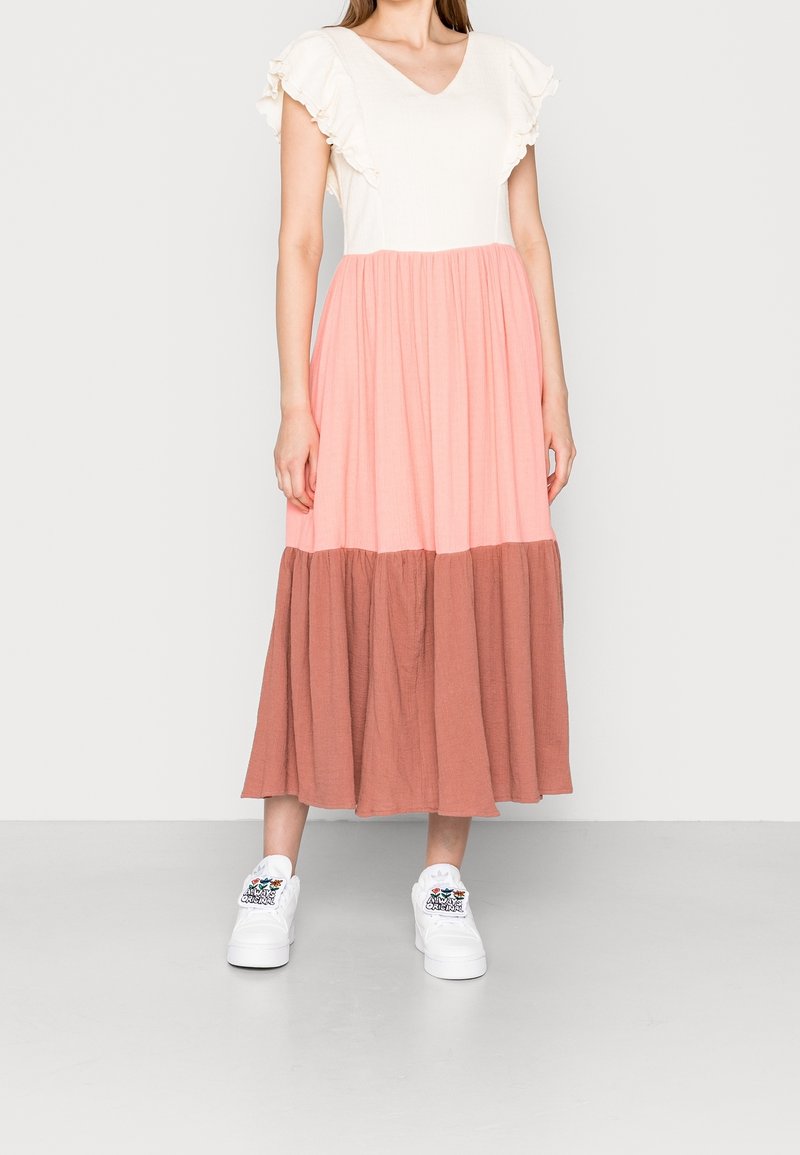 Abito maxi color block rosa e marrone con maniche corte a volant, scollo a V e una silhouette fluida, abbinato a sneakers bianche.
