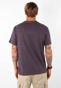 Camiseta de manga corta gris oscuro hecha de algodón, con un cuello redondo y un pequeño parche con el logo en el hombro. Textura suave.