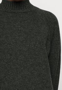 Pull en maille gris foncé avec un col haut côtelé et des manches longues. La texture est douce et légèrement duveteuse, affichant un tricot de moyenne épaisseur.