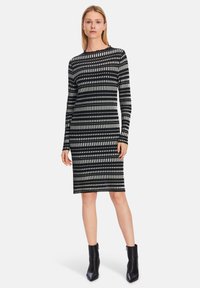 Schwarz-weißes Langarmkleid mit gestreiftem Muster, taillierter Form und rundem Halsausschnitt. Kombiniert mit schwarzen Stiefeletten.