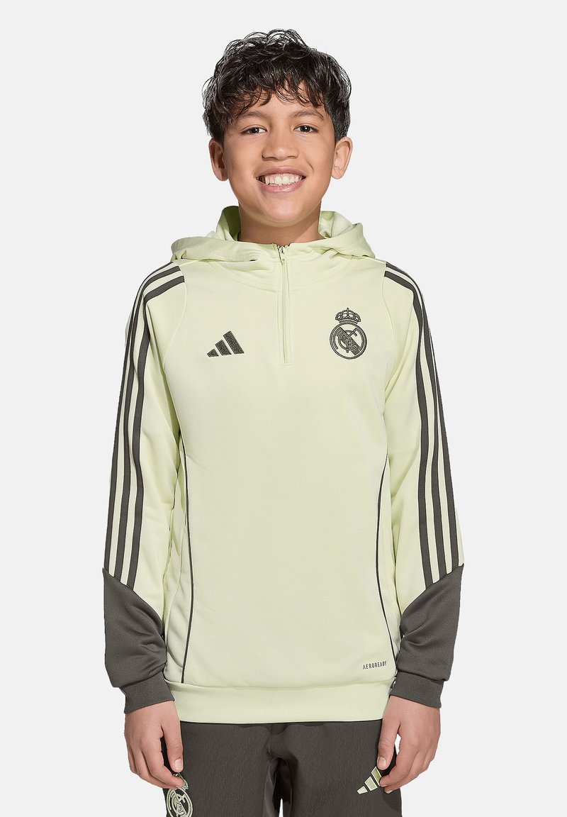Hoodie jaune pâle avec des accents gris et trois rayures noires sur les manches. Il présente un design zippé et un logo du Real Madrid sur la poitrine.