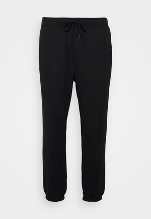 Pantaloni della tuta neri realizzati in materiale morbido con vita elastica e cordino regolabile. Dettagli alle caviglie con polsino e design leggermente affusolato.