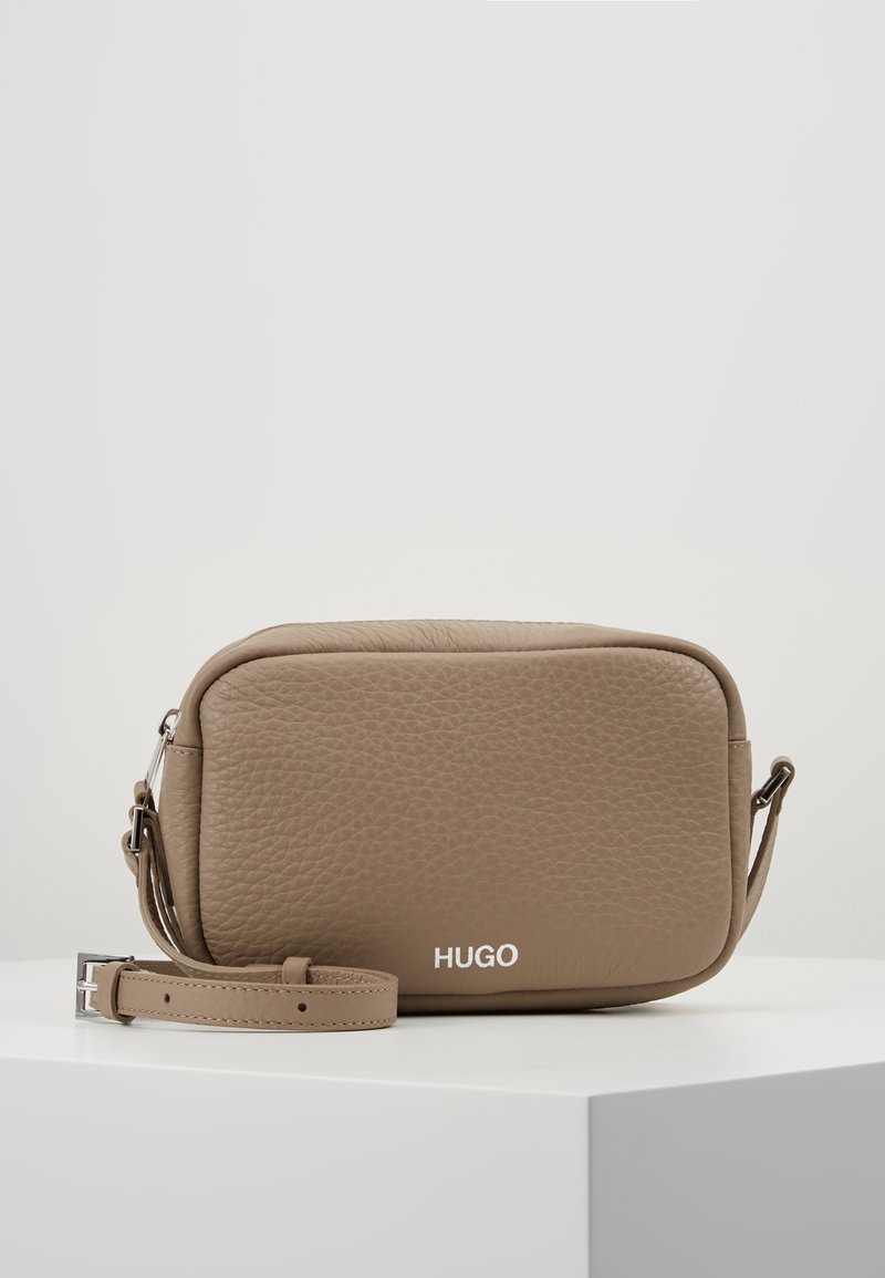Hnědá texturovaná kožená crossbody taška obdélníkového tvaru se stříbrn�ými detaily a logem "HUGO" na přední straně. Součástí je nastavitelné ramenní popruh.